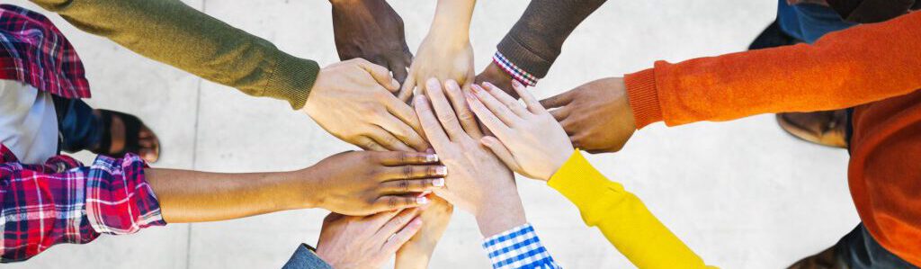 Teambuilding - Teamentwicklung- Foto von Händen, die im Kreis stehen und sich mit den Händen in der Mitte treffen